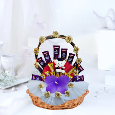 A delightful gift basket featuring 10 Cadbury Dairy Milk chocolates (11.2g each), 10 Five Star chocolates (16.8g each), a round handle basket adorned with mixed color paper and artificial roses, and a 4-inch Teddy Bear.