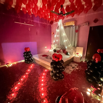 A room adorned with 40 heart-shaped balloons affixed to the ceiling, creatively suspended without helium. The ambiance is further enhanced by the soft glow of 30 small T-light candles scattered throughout the space.