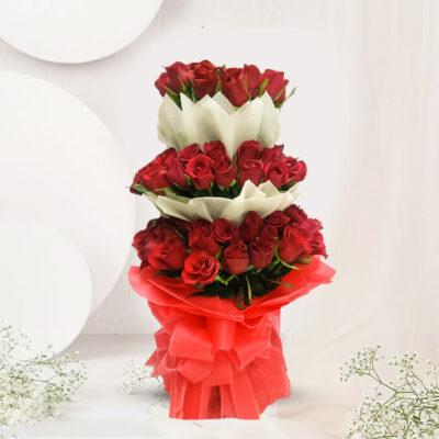 A stunning bouquet of 100 red Roses, adorned with red and white non-woven packing sheets, tied with a red net ribbon bow, and accented with lush green fillers