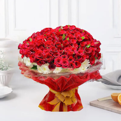 A lavish arrangement featuring 100 Red Roses, 40 White Gerberas, and lush green filler, elegantly presented in red jute packing paper with a golden ribbon bow.